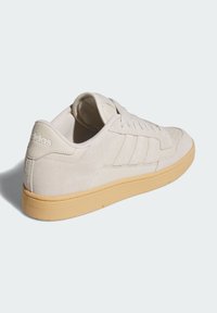 Bež sportska cipela od kože sa svijetlosmeđim gumenim potplatom. Sadrži tri bočne pruge, okrugli vrh i podstavljeni ovratnik. Diskretni logotip na peti.