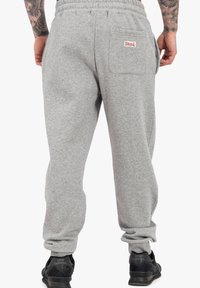 Šedé tepláky vyrobené z bavlneného zmesi s elastickým pásom, postrannými vreckami a zadným vreckom na nášivku s logom. Textúrovaná látka.