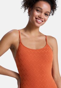 Débardeur orange texturé avec un motif en zigzag, présentant des bretelles fines et un décolleté rond. Tissu lisse, coupe ajustée.