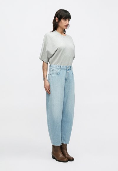 T-shirt gris oversize, jean bleu clair à jambes larges avec un motif délavé, et bottines marron à petit talon. Design simple, coupe décontractée.