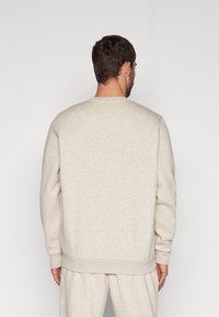 Sudadera de color beige claro con mangas largas, escote redondo y puños acanalados. Textura suave, diseño minimalista sin patrones ni logotipos visibles.