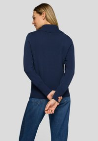 Marineblauer Strickpullover mit geripptem Saum und Bündchen, ausgestattet mit einem breiten, umgeschlagenen Kragen. Kombiniert mit blauen Denim-Jeans.