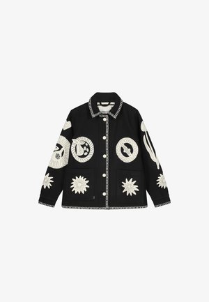 Zwarte jas met witte geborduurde patronen, waaronder sterren en planten. Voorzien van een knoopsluiting, grote zakken en een decoratieve kraag.