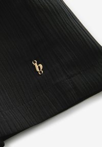 Zwarte textuurstof heeft een zichtbaar logo-accent in goudkleur. Het ontwerp bevat subtiele plooien en een netjes gestikte zoom.