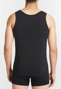 Canottiera nera in cotone morbido con scollo tondo e spalline larghe, indossata con pantaloni corti neri coordinati.
