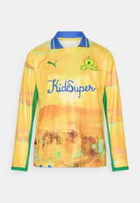 Maglia a maniche lunghe gialla con accenti verdi. Presenta un design astratto testurizzato e un colletto blu. Mostra in modo prominente il logo "KidSuper".