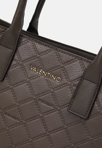 Brun läderhandväska med ett quiltat mönster, guld "VALENTINO"-logotyp och stadiga handtag. Märkbara sömnads- och textur detaljer finns.