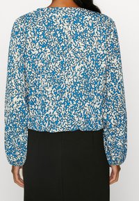 Blusa a maniche lunghe blu e bianca con motivo, taglio rilassato e scollatura rotonda, abbinata a un fondo nero monocromatico.