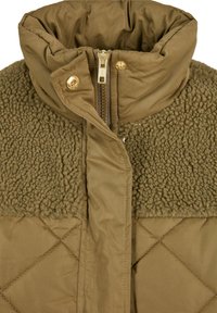 Gros plan sur le col d'une veste d'hiver vert olive avec tissu matelassé, doublure en polaire, fermeture éclair dorée et boutons-pression.