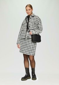 Houndstooth print jas en rok in zwart-wit tweed, gecombineerd met zwarte combat-stijl laarzen en een gestructureerde zwarte handtas.