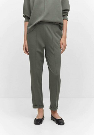 Olijfgroene tapering broek met een gladde textuur, voorzien van zijnaad en opgerolde boorden. Gecombineerd met zwarte platte schoenen.
