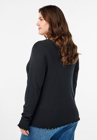 Must have musta varrukatega must särk, millel on narmastega serv ja mansetid, valmistatud pehmest kangast, nähtav küljelt valgel taustal.