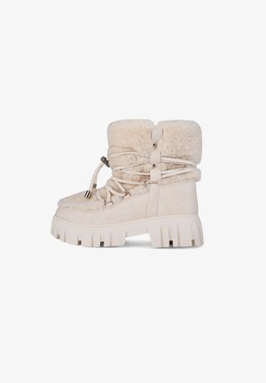 Beige suède enkellaarsjes met faux fur voering, dikke rubberen zool en vetersluiting. Voorzien van decoratieve banden en metalen accenten.