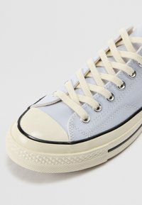 Baskets en toile bleu clair avec des lacets beige, un bout en caoutchouc et une bordure noire. Caractérisées par une semelle texturée avec un motif en diamant.