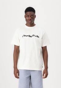 Weißes Baumwoll-T-Shirt mit einem schwarzen grafischen Design von laufenden Kaninchen auf der Brust. Kurze Ärmel und ein runder Ausschnitt.