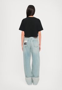 Μαύρο κοντό μπλουζάκι με κοντά μανίκια, συνδυασμένο με ανοιχτό μπλε ψηλόμεσο τζιν που έχει γραφικό πάνελ στις πίσω τσέπες.