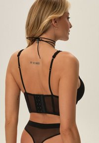 Czarny siatkowy stanik z usztywnianym tyłem, wyposażony w zapięcie na haftkę, regulowane ramiączka oraz delikatną fakturę.