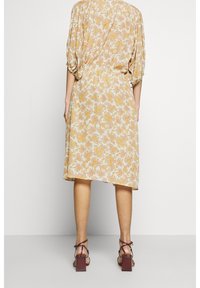Šaty s květinovým potiskem v světle žluté barvě, krátké nabírané rukávy, zúžený pas, volný střih, délka po kolena, v kombinaci s vínovými sandály na bloku.