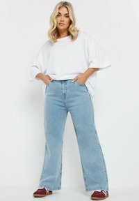 Lichtblauwe high-waisted jeans met een ontspannen pasvorm en wijde pijpen, gecombineerd met een losse witte t-shirt en bordeauxrode schoenen.