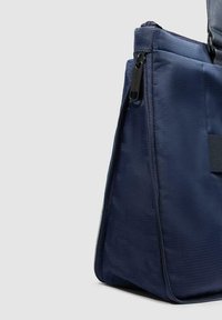 Bolsa de tela azul marino con forma estructurada, con cierre de cremallera y detalles de superficie texturizada. Diseño compacto y versátil.