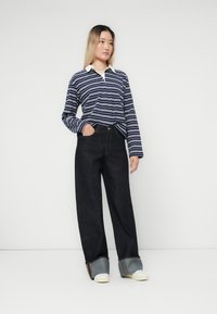 Marineblå og hvit stripete langermet polo skjorte med hvit krage, kombinert med høyt liv mørk denim vide ben jeans og hvite sneakers.