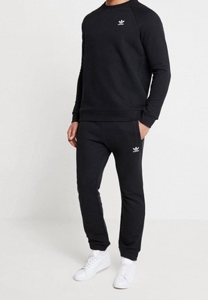 Completo felpa nera e pantaloni della tuta realizzati in tessuto morbido, con un piccolo logo bianco sul petto e sulla gamba dei pantaloni, con polsini a coste e una vestibilità rilassata.