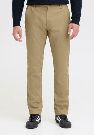 Beige cotton trousers with a straight leg design, featuring side pockets and a belt loop, paired with black athletic shoes.