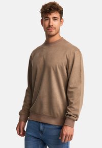 Bruine sweatshirt met lange mouwen, geribbelde halslijn en boorden. Zachte textuur; gecombineerd met blauwe jeans; minimalistisch ontwerp.