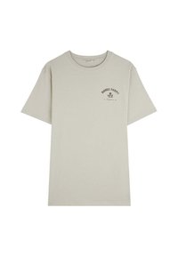 Camiseta de algodón color beige claro con mangas cortas y un cuello redondo. Presenta un pequeño texto gráfico negro en la parte superior izquierda del pecho.