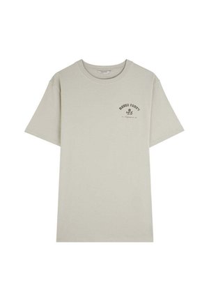 Camiseta de algodón color beige claro con mangas cortas y un cuello redondo. Presenta un pequeño texto gráfico negro en la parte superior izquierda del pecho.