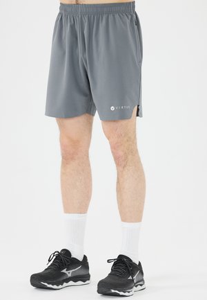 Mand iført grå træningsshorts med Virtus-logo, hvide crew-sokker og sorte løbesko, står på en hvid baggrund.