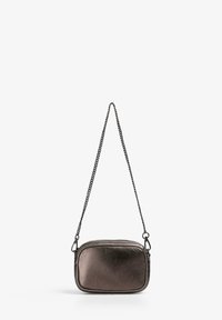 Pequeño bolso cruzado rectangular metálico gris con una parte superior con cremallera y una larga cadena negra colgando sobre un fondo blanco.