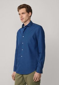 Camisa de manga larga azul con cuello abotonado, hecha de tejido tejida, con botones blancos y un dobladillo recto.