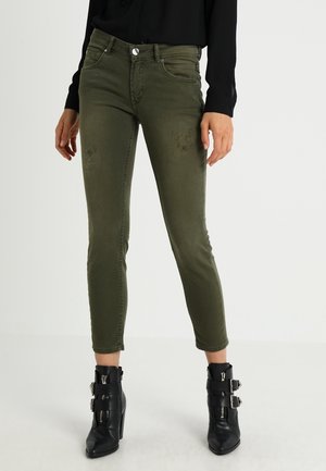 Jeans skinny vert olive avec des détails usés subtils, associés à des bottines noires à boucles avec une finition texturée.