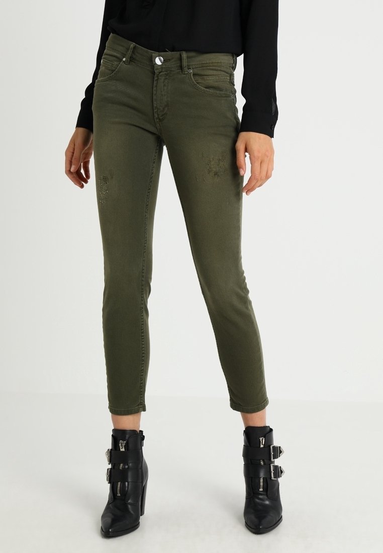 Jeans ajustados en verde oliva con sutiles detalles desgastados, combinados con botas negras hasta el tobillo con hebillas y un acabado texturizado.