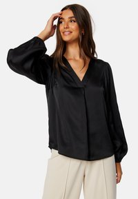 Blusa nera in satin con scollatura a V, maniche voluminose e vestibilità rilassata. Tessuto liscio con una leggera lucentezza e polsini arricciati.