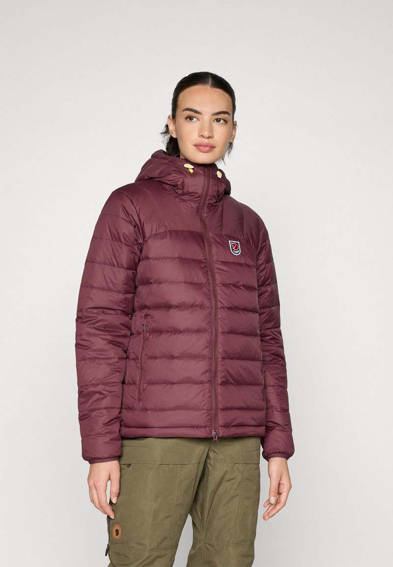 Burgundska puffer jakna tamne boje s kapuljačom, zatvaranjem na zip i podignutim ovratnikom; sadrži logotip i žute snap detalje.