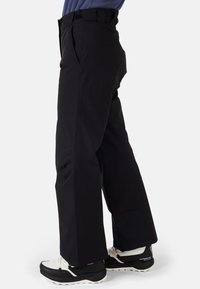 Svarta vattenavisande byxor med en lös passform, som har en bred bendesign, bältesöglor och förstärkta lappar på underbenen, kombinerat med svarta och vita sneakers.