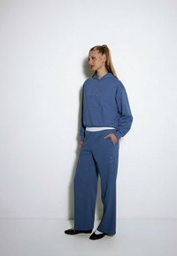 Niebieska bawełniana bluza z kapturem z detalem w kształcie gwiazdy oraz dopasowanymi szerokimi spodniami. Posiada kieszeń z przodu oraz luźny krój, zestawiona z ciemnym obuwiem.