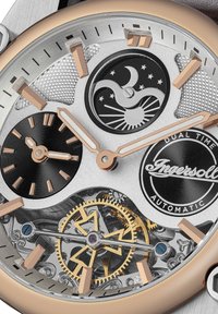 Automatisch horloge met zilver en roségouden afwerking, met een dubbele tijdsaanduiding, ingewikkelde tandwielen, een gestructureerde zwarte wijzerplaat en gedetailleerde uurmarkeringen.