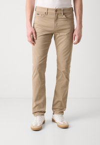 Beige, slim-fit chino's van katoen. Voorzien van een knoopsluiting, voor- en achterzakken, en een klein logopatch op de tailleband.