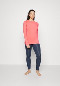 Langermet atletisk topp i knallrosa og marineblå tights. Laget av pustende stoff med glatt tekstur og tettsittende design.