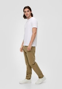 Weißes T-Shirt mit kurzen Ärmeln, beige Chinos und weiße Sneaker. Das Shirt ist schlicht und die Hose hat einen geraden Schnitt mit Seitentaschen.