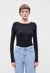 Μαύρο ριχτό τοπ με μακριά μανίκια και στρογγυλή λαιμόκοψη, συνδυασμένο με ανοιχτό μπλε παντελόνι ψηλής μέσης με κλασικό σχέδιο πέντε τσεπών.