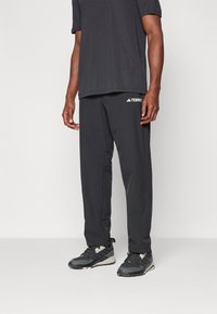 Pantalons de sport noirs avec une coupe ample, arborant un logo discret sur la cuisse gauche, associés à un t-shirt noir à manches courtes et des baskets noires.