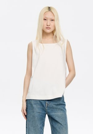 Weißes ärmelloses Oberteil aus weichem Stoff, mit quadratischem Ausschnitt und Knopfdetails am Saum, kombiniert mit lockeren blauen Jeans.