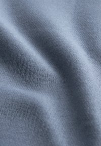 Tissu tricoté bleu clair doux avec une texture fine visible et des plis subtils créant des ombres douces.