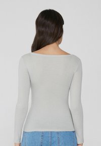 Haut à manches longues côtelé gris clair avec un décolleté bateau, design ajusté et texture douce, associé à un short en denim taille haute.