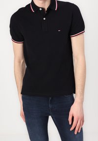 Svart polo t-shirt i bomull, med en treknapps placket, skräddarsydd passform och vita och röda randiga detaljer på kragen.