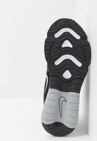 Černá a šedá atletická podrážka obuvi s texturovaným povrchem, výraznými drážkami a bílým logem. Použitý odolný gumový materiál.